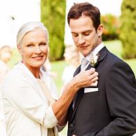 Portrait of happy mother pinning corsage on groom's suit at outdoor wedding. Horizontal shot.
