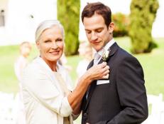 Portrait of happy mother pinning corsage on groom's suit at outdoor wedding. Horizontal shot.