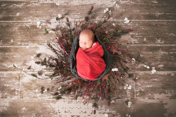 A portrait of a newborn baby wrapped in Christmas themed cheesecloth and crochet wrap.