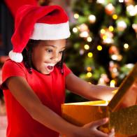 Cute African-American girl wearing Santa's hats is opening Christmas presents.   