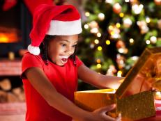 Cute African-American girl wearing Santa's hats is opening Christmas presents.   