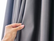 close-up of a woman's hand touching the curtain, gray blackout fabric, light-blocking fabric