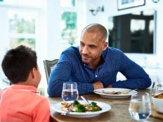 Mature man leaning forward towards boy, food on dining room table, family meal time, conversation, bonding