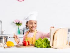 cheerful african american kid in apron and chef hat cooking on kitchen