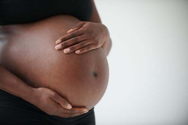 Midsection of pregnant Black woman holding belly