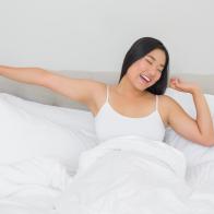 Smiling woman lying in bed stretching in the morning at home in bedroom