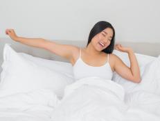 Smiling woman lying in bed stretching in the morning at home in bedroom