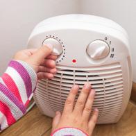 Child's hands adjusts the temperature of the electric fan heater at home in winter time. Cropped image, selective focus.