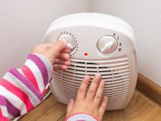 Child's hands adjusts the temperature of the electric fan heater at home in winter time. Cropped image, selective focus.