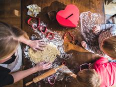 A stock photo of a woman baking Valentines day heart shaped sugar cookies with her identical twin sons.