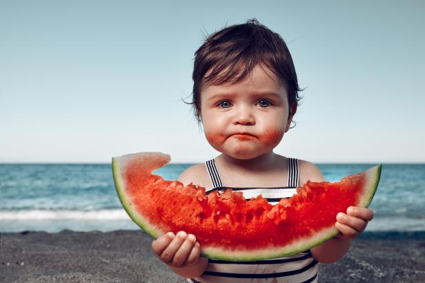 funny little girl on the beach eating watermelon and making funny face.
