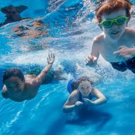 Three children swimming underwater, smiling at the camera.