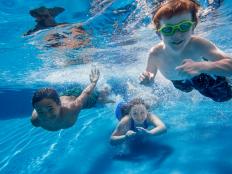 Three children swimming underwater, smiling at the camera.