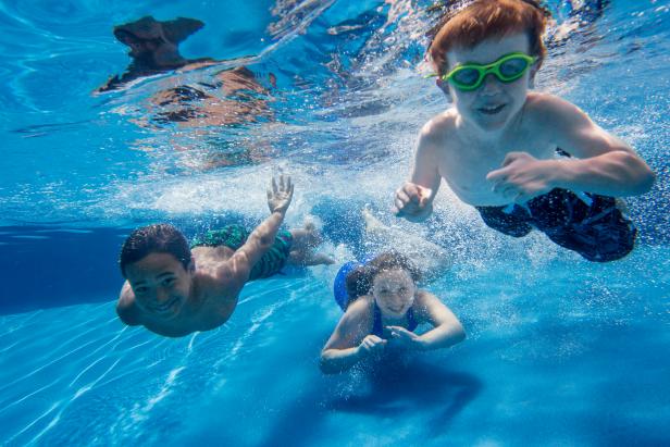 Three children swimming underwater, smiling at the camera.