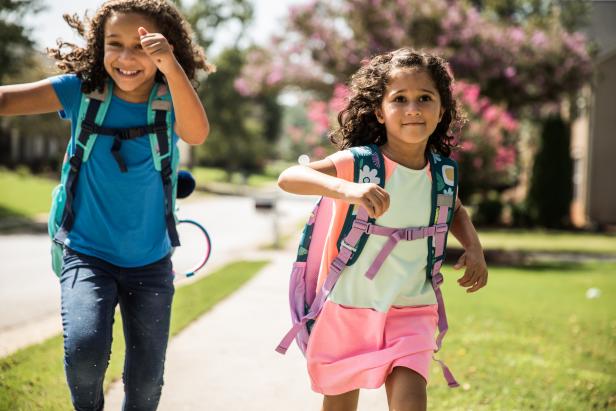 Young girls running outside wearing backpacks