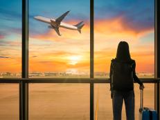 Travel tourist standing with luggage watching sunset at airport window. Woman looking at lounge looking at airplanes while waiting at boarding gate before departure. Travel lifestyle. Transport and travel concept