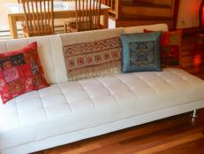 Colorful throw pillows adorn a white leather sofa in the living room/dining room of a cottage.