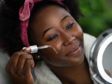 Beautiful young woman applying face serum on her face.