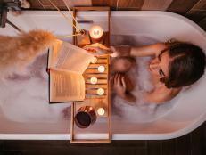 High angle view of a young woman reading in a bathtub, turning page, enjoying time with herself. Candles and red wine. Valentines day concept, International womans day