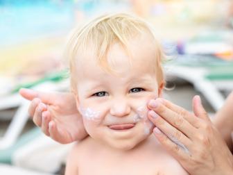 Mother applying sunscreen protection creme on cute little toddler boy face. Mom using sunblocking lotion to protect baby from sun during summer sea vacation. Children healthcare at travel time.