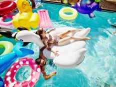 Laughing woman floating on large inflatable pool toy in outdoor pool during pool party with swimming friends and different pool toys in background