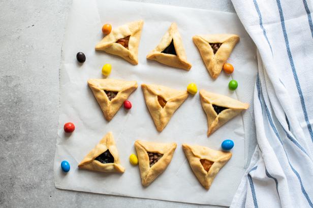 Top view hamantaschen cookies and colorful candies on a baking paper with napkin on a gray background.