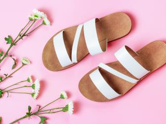 A pair of white sandals and flowers on a pink background top view.