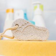 Pumice stone in foot shape on yellow bath sponge. Bathroom objects. Pedicure essentials.