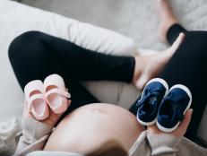 Overhead view of Asian pregnant woman holding a pair of blue and pink baby shoes in front of her belly. Expecting a new life, mother-to-be, gender reveal concept