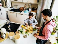 A father and son are in the kitchen at home preparing a salad for lunch together.