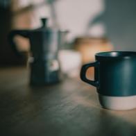 Blue coffee cup on wooden table with coffee maker in morning sunshine