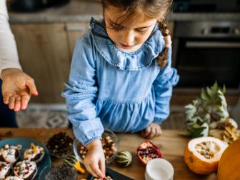 Young woman and her little cute daughter are cooking in kitchen. Having fun together while making and decorating muffins and cookies for autumn celebration.