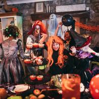 Group of young friends dressed in costumes dancing and playing together at a Halloween party. One of their parents is playing alongside them, also dressed in a costume.