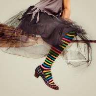 image of a woman dressed like a witch with colorful striped panties and sitting in a flying bloom ,Grey background