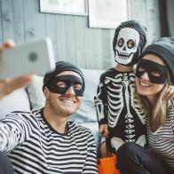 Young parents with baby boy celebrating Halloween at home. They ware costumes, playing around in living room and take selfies