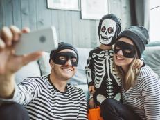 Young parents with baby boy celebrating Halloween at home. They ware costumes, playing around in living room and take selfies