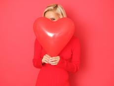 Happy woman with red heart shape balloon isolated on red background.