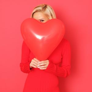 Happy woman with red heart shape balloon isolated on red background.