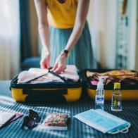 Woman packing suitcase for summer trip, including face masks and travel-sized antibacterial hand gels