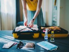 Woman packing suitcase for summer trip, including face masks and travel-sized antibacterial hand gels