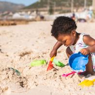 Cute little African girl playing with a sand pail and shovel during a sunny day at the beach in summer