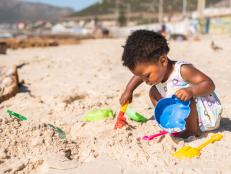 Cute little African girl playing with a sand pail and shovel during a sunny day at the beach in summer