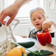 Close-up of a little girl in the kitchen at home helping her mother sort fresh bought vegetables