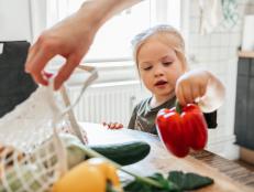 Close-up of a little girl in the kitchen at home helping her mother sort fresh bought vegetables