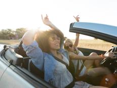 Young women singing and having fun on road trip with convertible car.