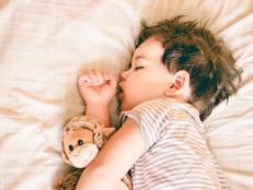 Boy sleeping on bed holding a soft toy by his side, against a soft cream background.