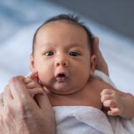 Close up photo of a one week old baby boy with dark hair and eyes open, mixed race, Asian and Caucasian. Australia