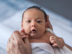 Close up photo of a one week old baby boy with dark hair and eyes open, mixed race, Asian and Caucasian. Australia