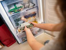 Girl taking bag with frozen mixed vegetables from refrigerator.
