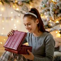 Happy teenage girl in pajamas and antler headband opening Christmas present